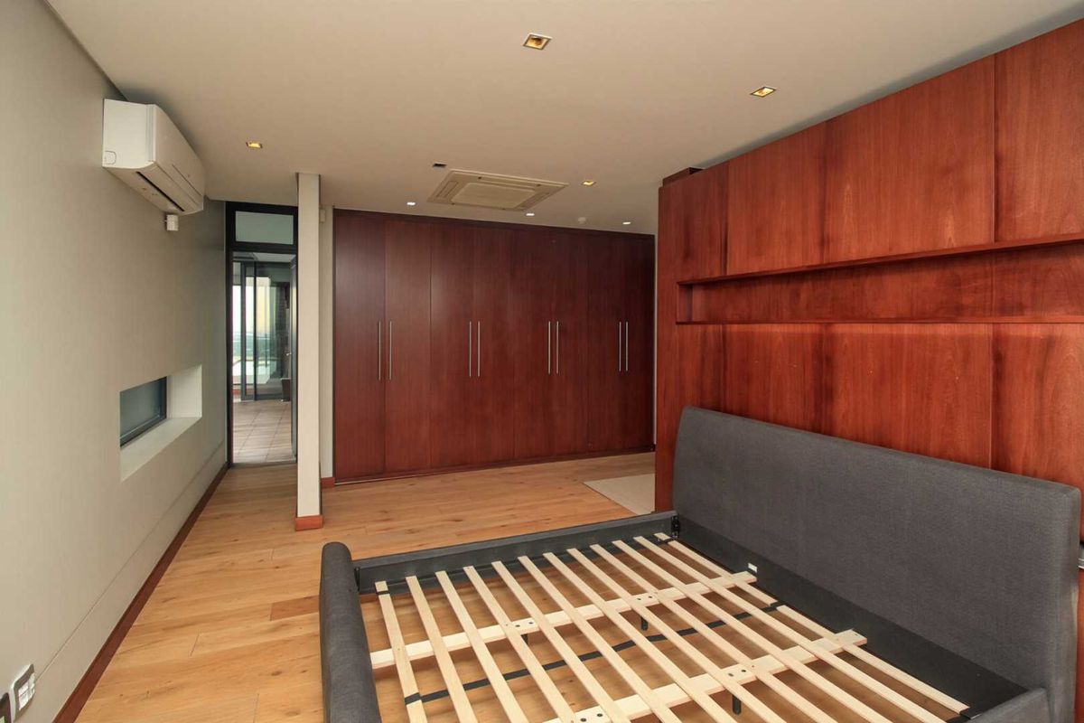 Spacious bedroom featuring extensive built-in wooden cabinetry, recessed ceiling lighting, integrated air conditioning unit, and light-toned hardwood flooring.