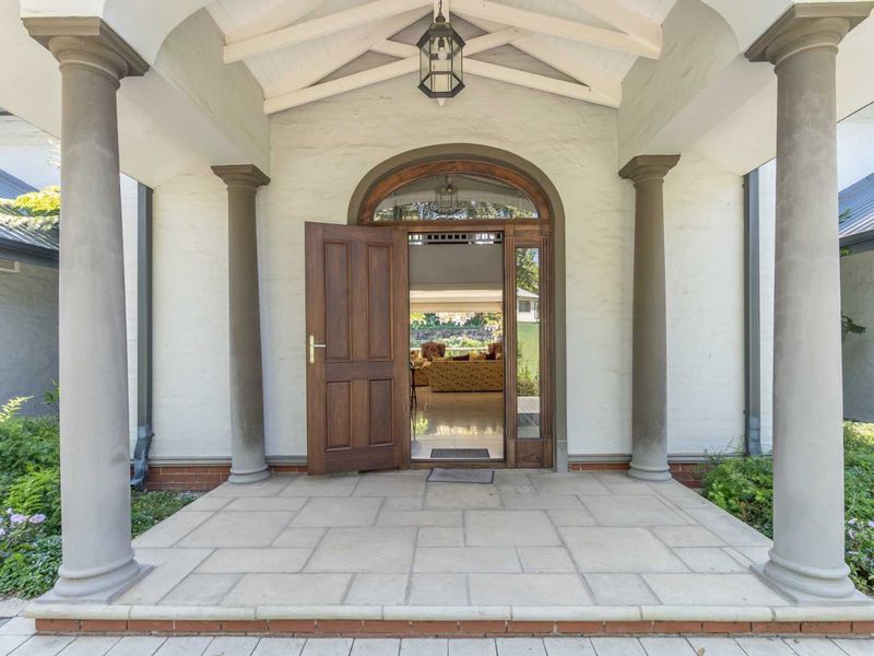 Elegant covered entrance porch featuring stone columns, arched timber door, and exposed rafters, providing a welcoming and sophisticated entry to the home.