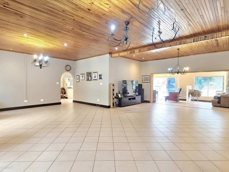 Spacious open-plan living area featuring a warm timber ceiling, neutral tiled flooring, and multiple wrought iron chandeliers, leading out to a patio area.