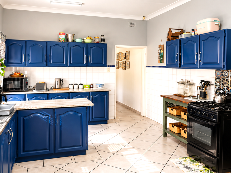 A functional kitchen featuring blue cabinetry, laminate countertops, a double stainless steel sink, and a freestanding gas oven with tiled splashbacks.