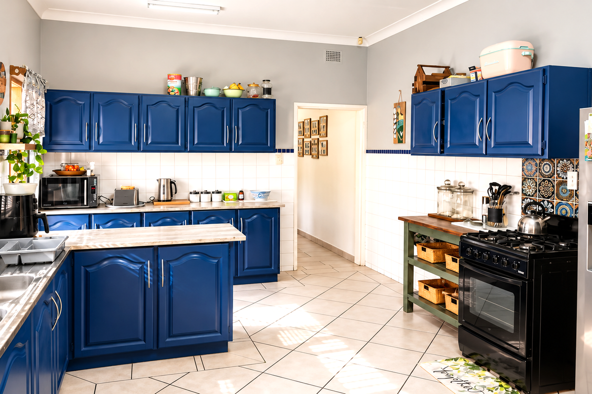 A functional kitchen featuring blue cabinetry, laminate countertops, a double stainless steel sink, and a freestanding gas oven with tiled splashbacks.