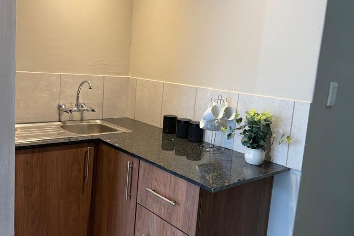 A compact kitchen area featuring wood-finish cabinetry, granite countertops, and a stainless steel sink with a wall-mounted faucet.