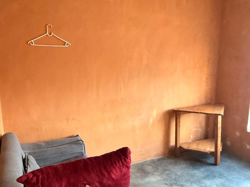 A small bedroom space featuring textured orange walls and a concrete floor, requiring cosmetic updates to improve the overall finish and appeal.