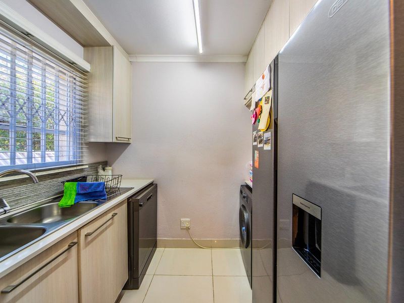 A functional scullery featuring laminate cabinetry, a double bowl stainless steel sink, tiled flooring, and space for laundry appliances.