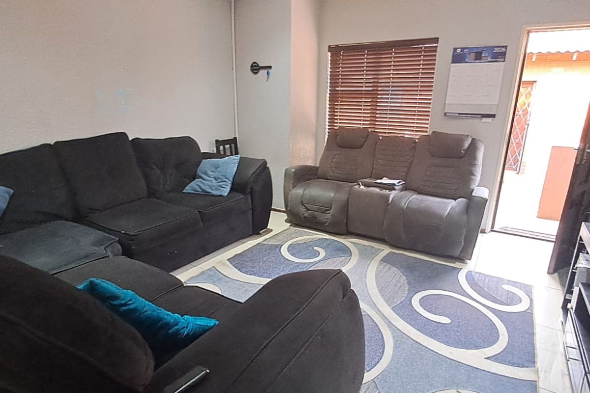 A functional living room featuring tiled flooring, horizontal window blinds, and direct access to an outdoor area through a standard door.