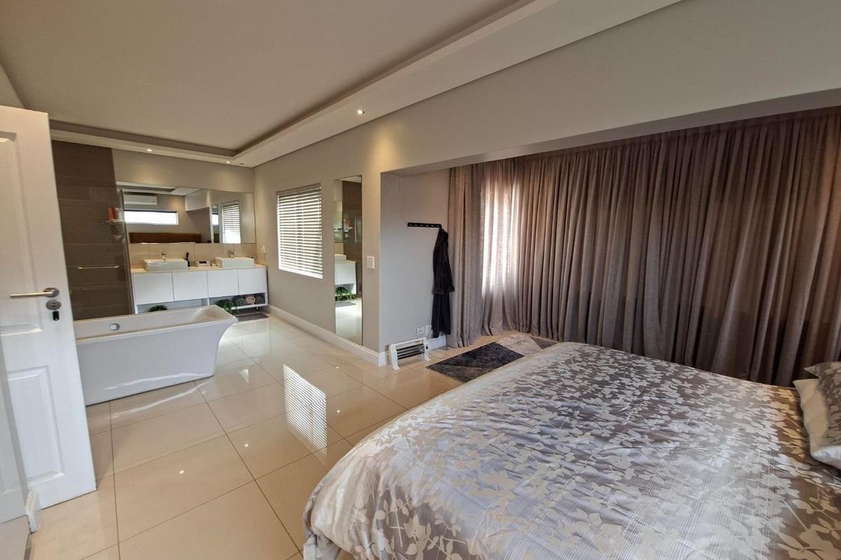 Spacious bedroom featuring an open-plan en-suite bathroom with a freestanding bathtub, double vanity, and modern tiled flooring.