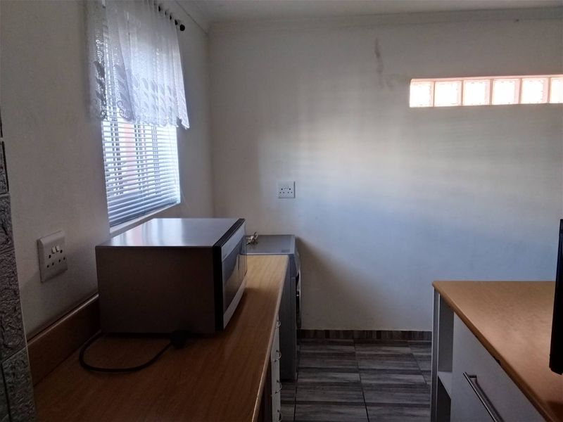 A functional kitchen area featuring laminate countertops, tiled flooring, and a glass block window, showing signs of minor wall staining.