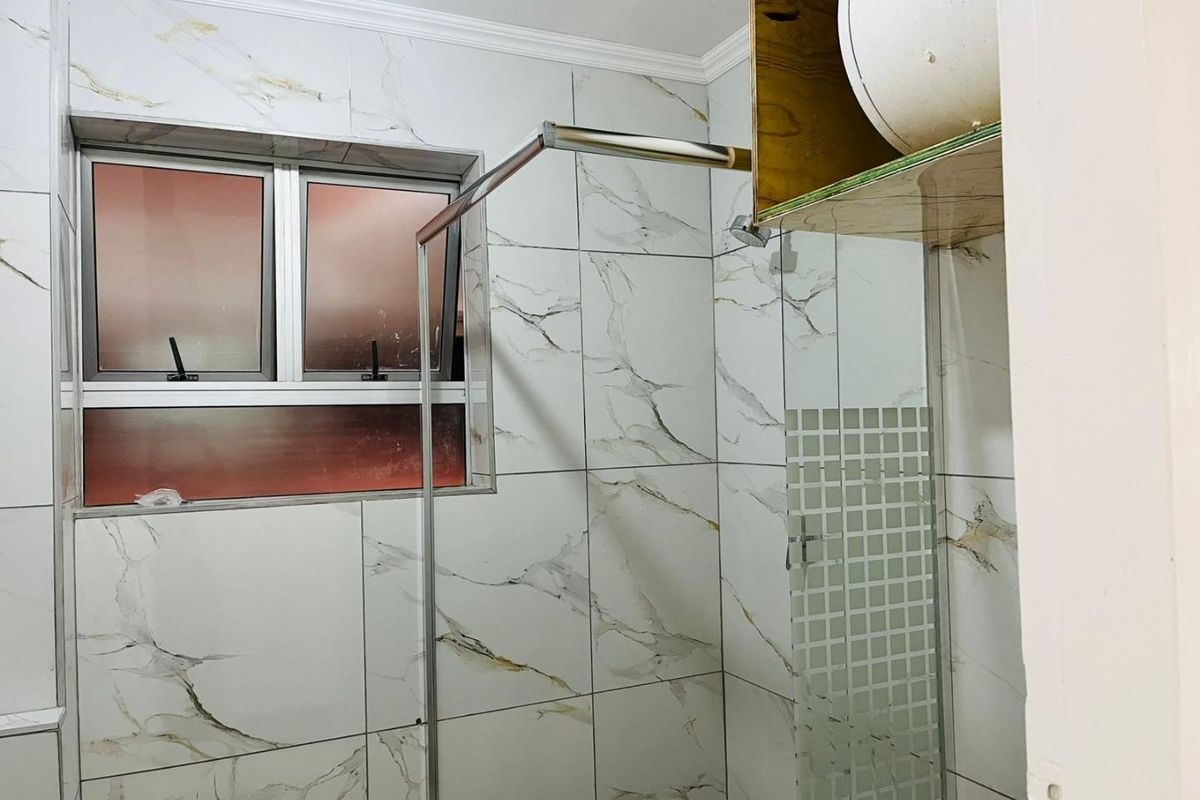 A modern bathroom featuring marble-look wall tiles, an aluminium window, and a glass shower screen with built-in shelving.