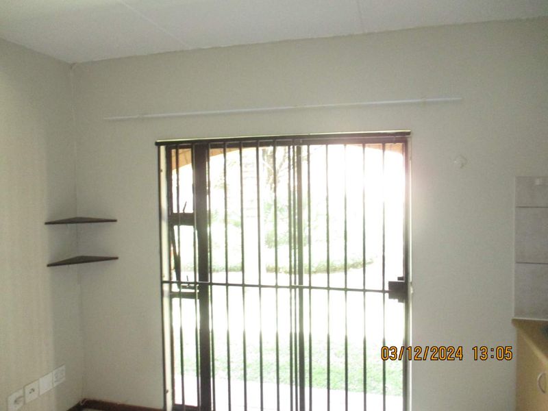 An empty living area featuring a sliding door with security bars, built-in shelving, and a curtain rod, requiring minor cosmetic updates.