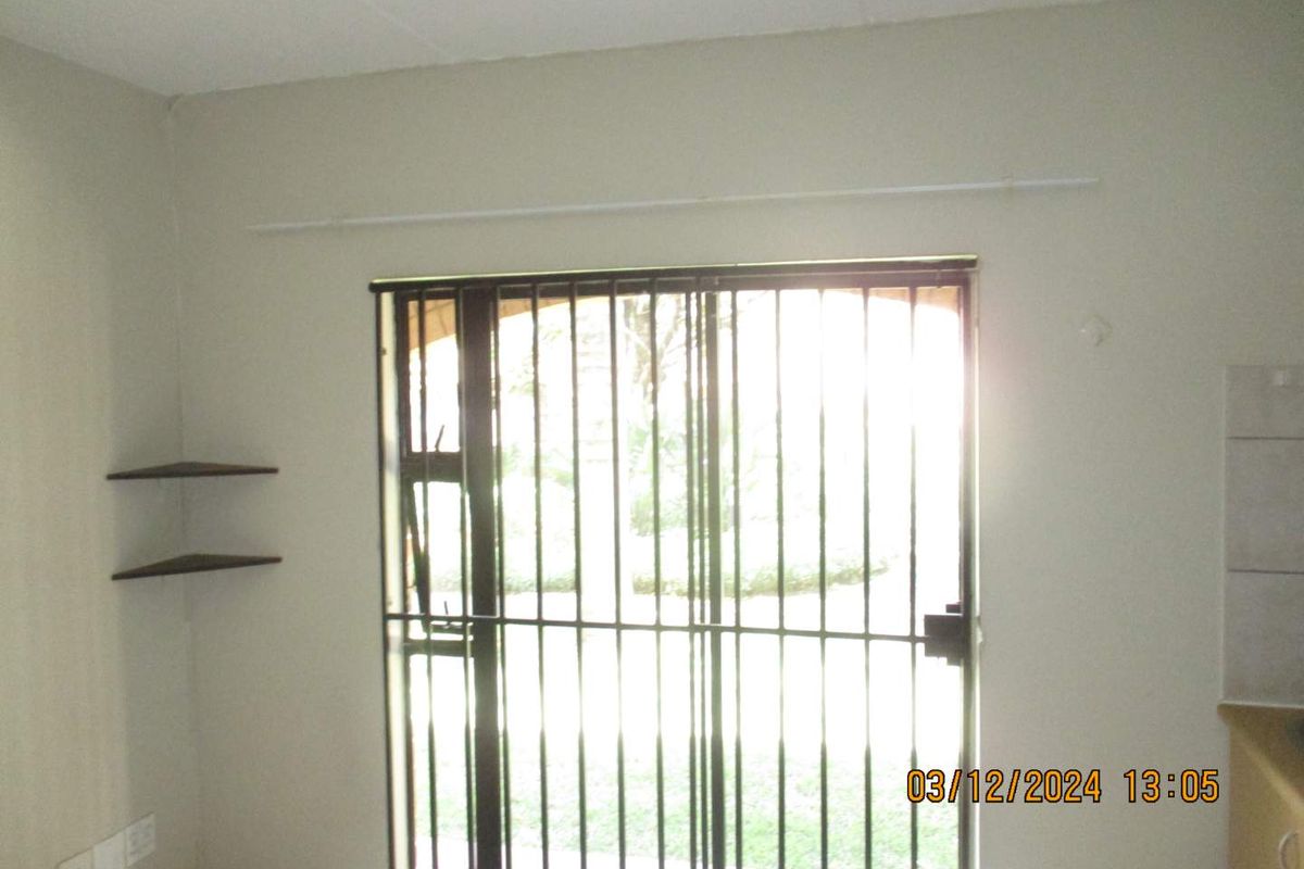 An empty living area featuring a sliding door with security bars, built-in shelving, and a curtain rod, requiring minor cosmetic updates.