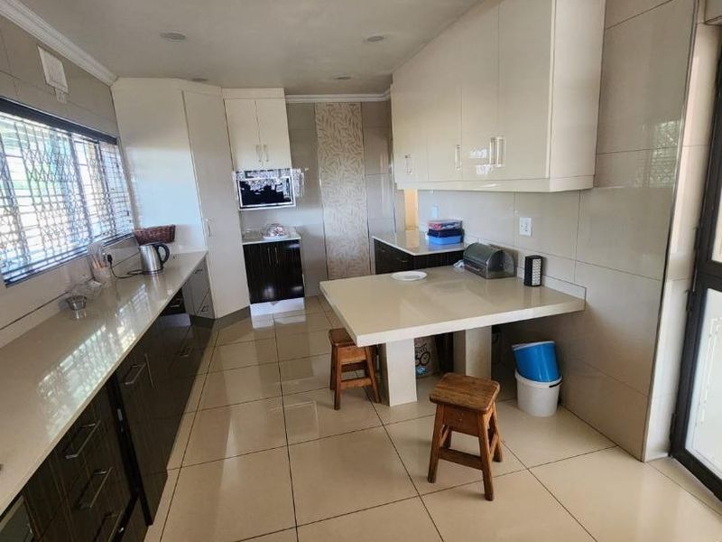 Modern kitchen featuring high-gloss cabinetry, stone countertops, and a breakfast bar, with tiled flooring throughout.