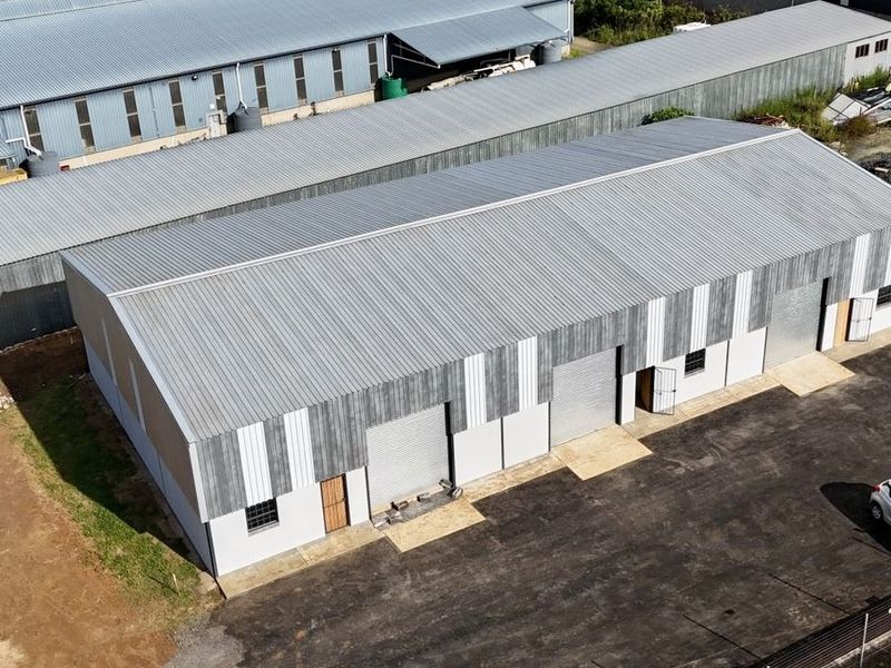 Aerial view of an industrial warehouse complex featuring corrugated metal roofing, multiple roller shutter doors, and a paved driveway area.