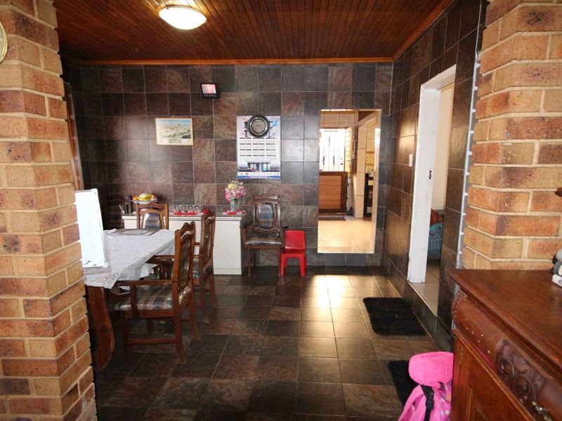 Dining area featuring exposed brick columns, dark ceramic wall and floor tiling, and a timber-paneled ceiling.