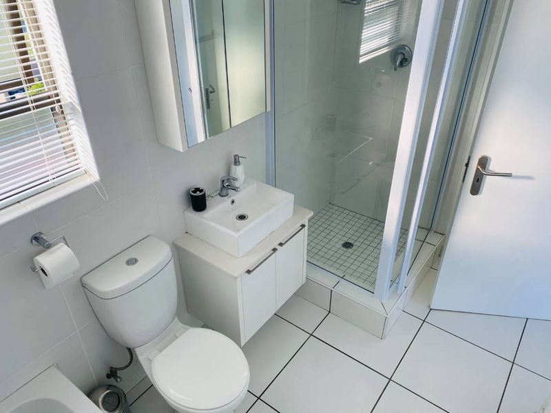 A clean, modern bathroom featuring a glass-enclosed shower, white vanity with basin, mirrored medicine cabinet, and neutral tiled finishes throughout.