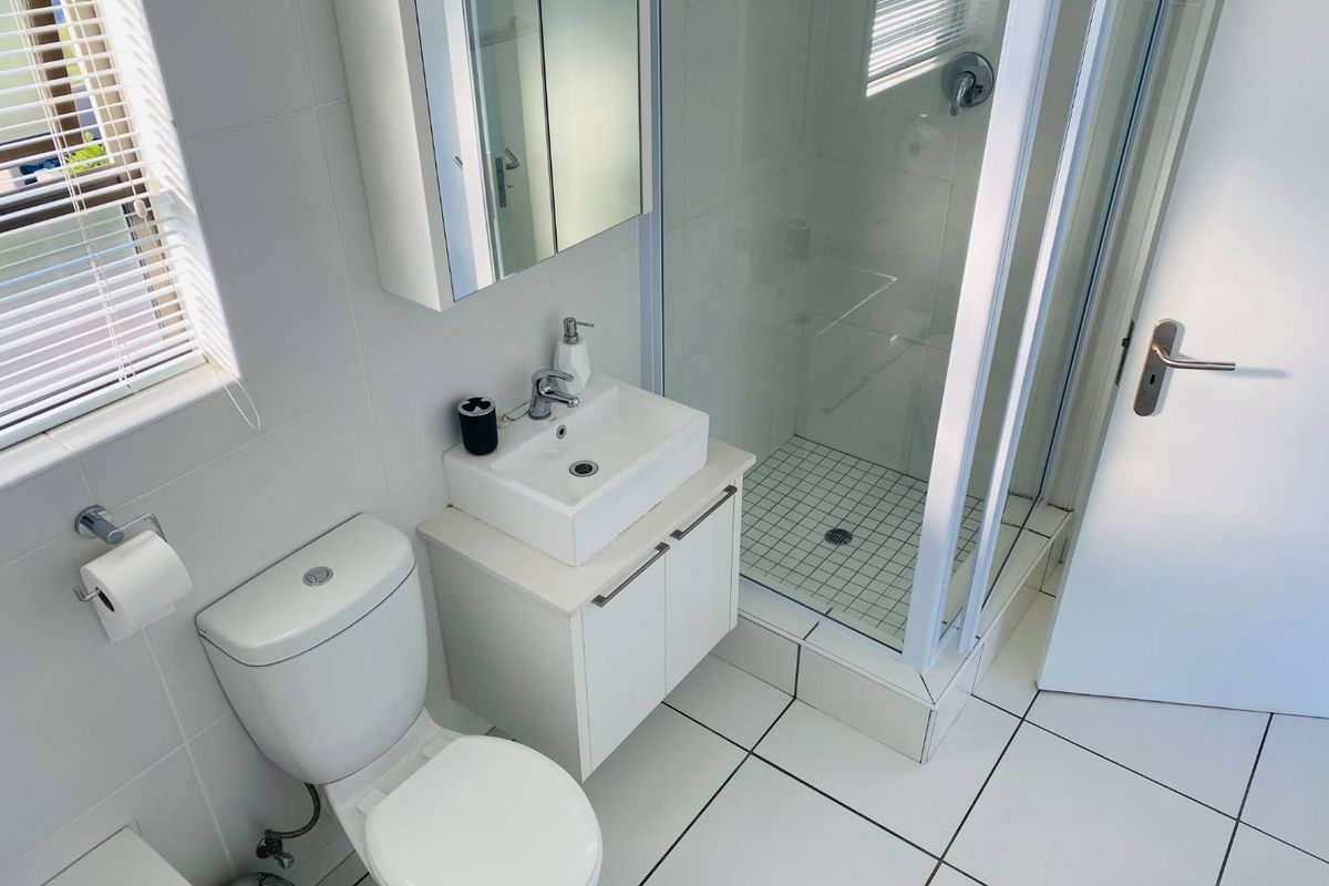 A clean, modern bathroom featuring a glass-enclosed shower, white vanity with basin, mirrored medicine cabinet, and neutral tiled finishes throughout.