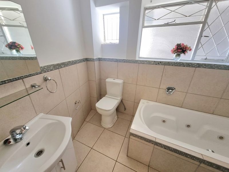 A clean, well-maintained bathroom featuring a built-in jetted bathtub, a vanity sink, and neutral wall and floor tiling.