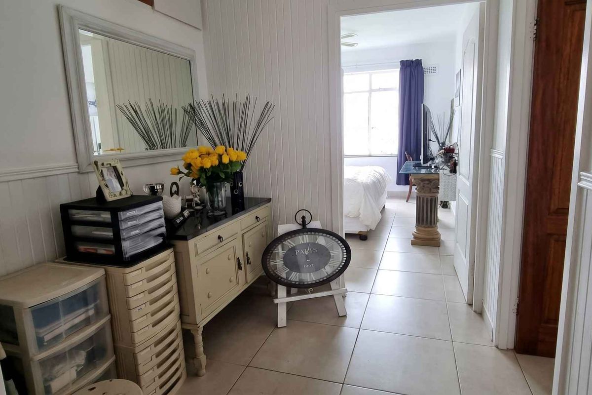 A view from the hallway looking into a bedroom, featuring tiled flooring and classic wainscoting wall paneling.