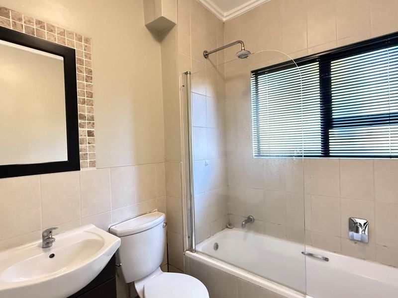 A clean, functional bathroom featuring a bathtub with an integrated shower, glass screen, pedestal basin, and neutral wall tiling.