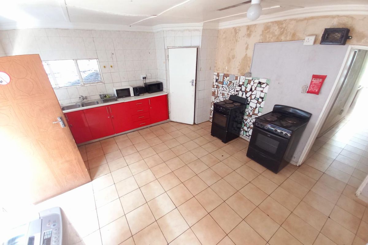 A dated kitchen featuring red cabinetry, tiled flooring, and dual freestanding stoves, requiring significant cosmetic updates and wall repairs.