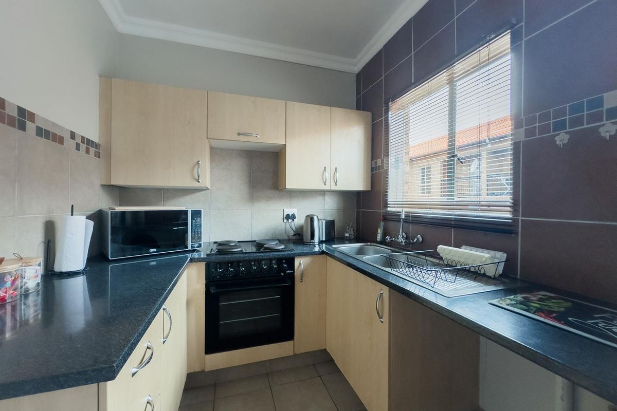 A functional kitchen featuring light wood cabinetry, dark laminate countertops, a built-in oven and hob, and tiled finishes throughout.