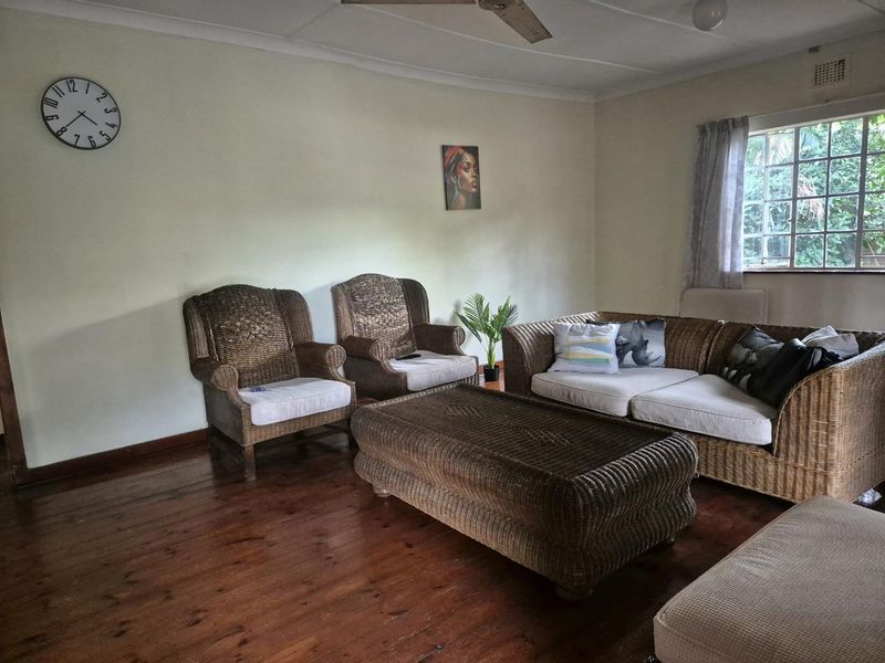 A living room featuring polished hardwood flooring, a ceiling fan, and natural light from a window.