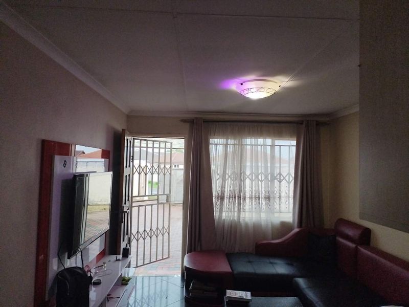 A living room featuring tiled flooring, ceiling coving, and a security gate at the entrance, providing access to the exterior.