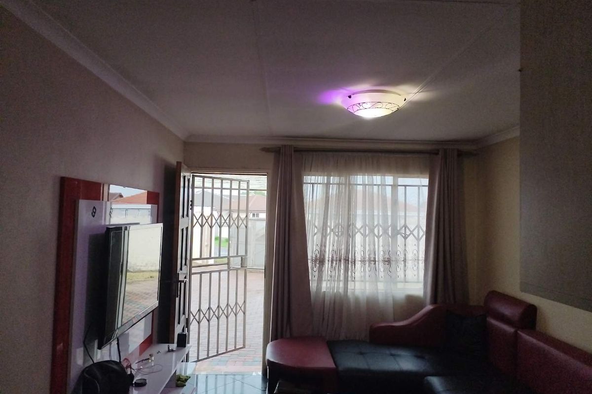 A living room featuring tiled flooring, ceiling coving, and a security gate at the entrance, providing access to the exterior.
