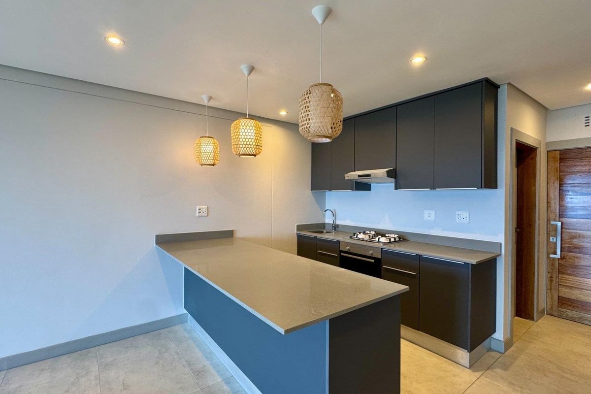 Modern kitchen featuring dark cabinetry, stone countertops, gas hob, under-counter oven, and integrated extractor fan with a breakfast bar island.
