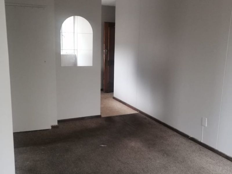 An empty living room featuring an arched wall opening and carpeted flooring, requiring cosmetic updates and new flooring to improve its overall condition.