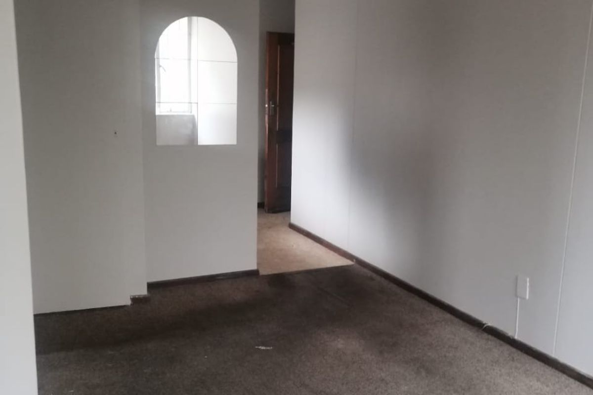 An empty living room featuring an arched wall opening and carpeted flooring, requiring cosmetic updates and new flooring to improve its overall condition.