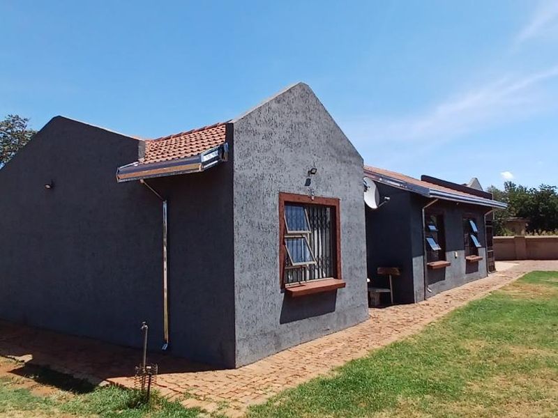 Rear view of the house featuring a textured plaster facade, tiled roof, and a paved walkway surrounding the building with a surrounding boundary wall.