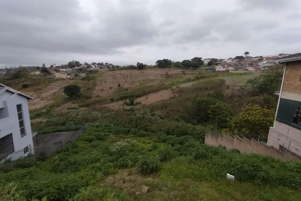 An elevated view of a vacant residential plot featuring sloped terrain and surrounding neighborhood development.