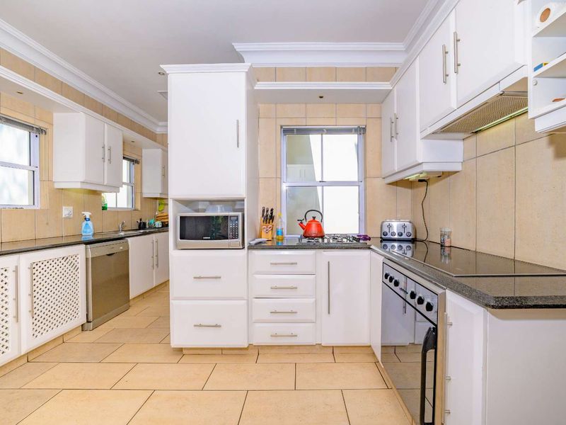 A well-maintained kitchen featuring white cabinetry, granite countertops, tiled flooring, and integrated appliances including an oven, hob, and extractor fan.