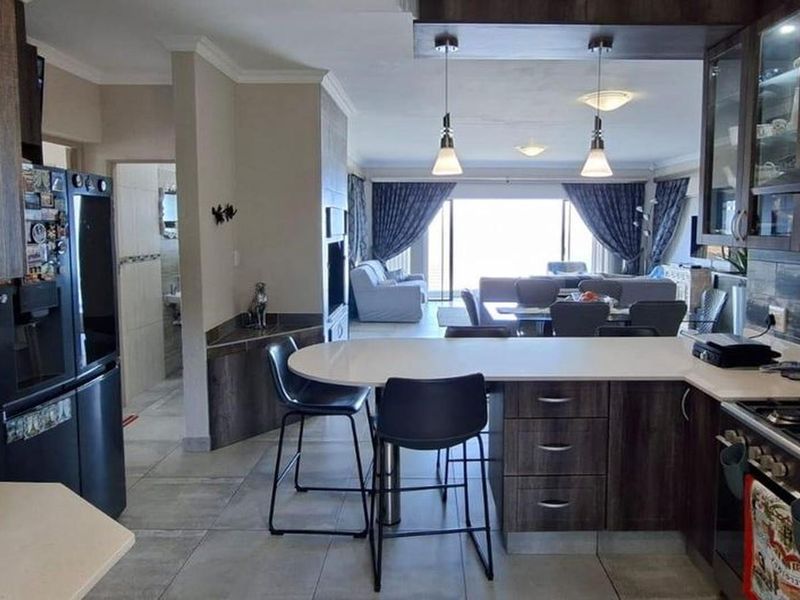 Spacious open-plan kitchen and living area featuring modern cabinetry, stone countertops, a gas hob, and tiled flooring, flowing into a bright lounge space.