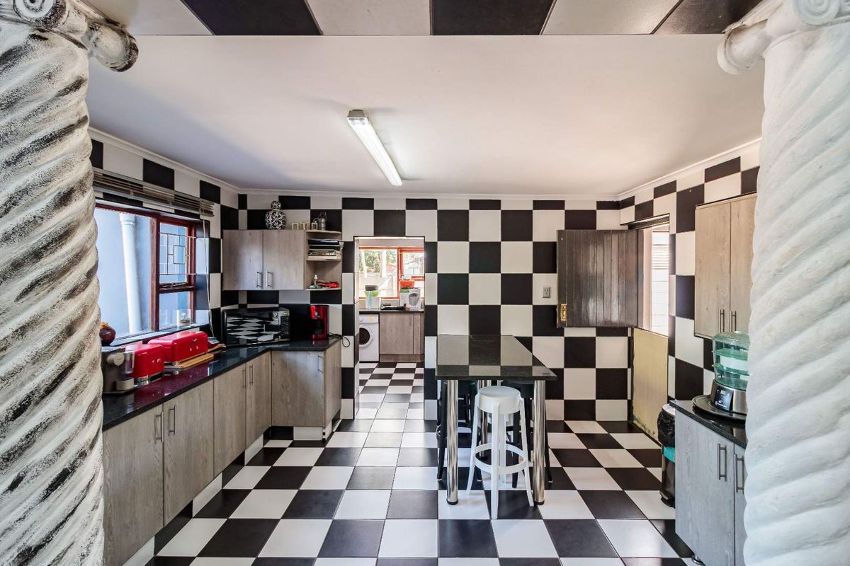 A kitchen featuring a bold black and white checkerboard theme with wood-grain cabinetry, granite countertops, and an adjacent scullery area.