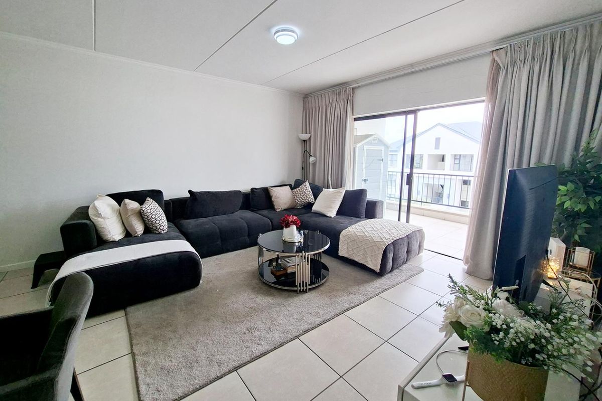 A bright and spacious living room featuring large sliding glass doors that open onto a private balcony, finished with neutral floor tiles.