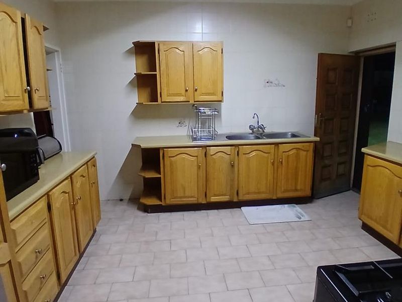 A functional kitchen featuring wooden cabinetry, tiled flooring, and a double basin sink, offering a clean and practical workspace.