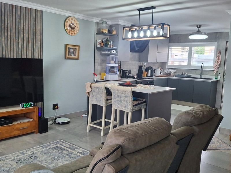 An open-plan living and kitchen area featuring modern cabinetry, a central kitchen island, tiled flooring, and contemporary pendant lighting.