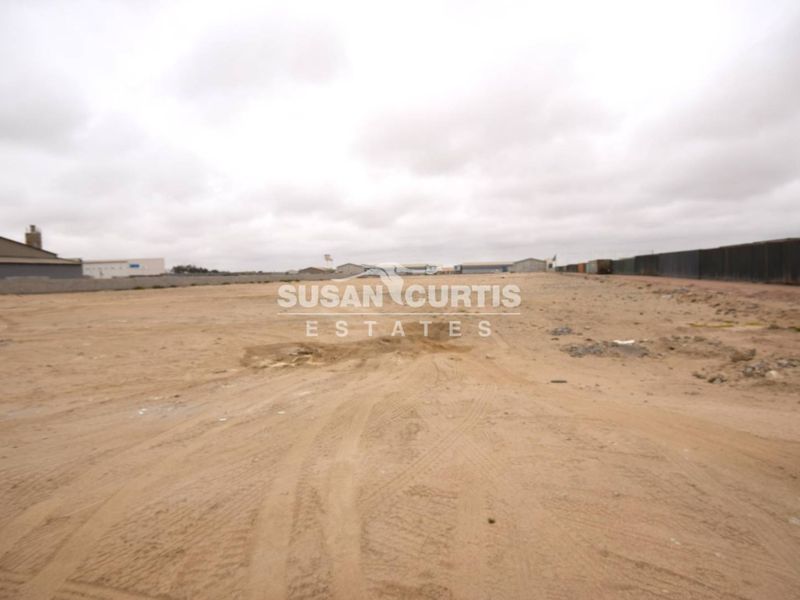 A wide-angle view of a vacant commercial land plot featuring level ground and perimeter fencing, suitable for industrial or commercial development.