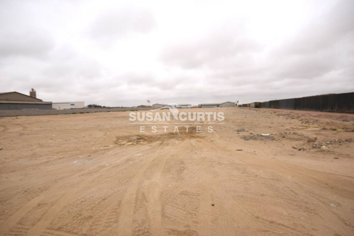 A wide-angle view of a vacant commercial land plot featuring level ground and perimeter fencing, suitable for industrial or commercial development.