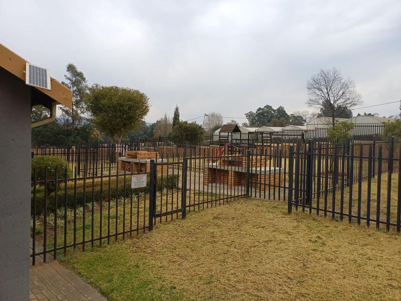 Communal garden area featuring brick braai facilities, secure steel perimeter fencing, and a paved walkway within the apartment complex grounds.