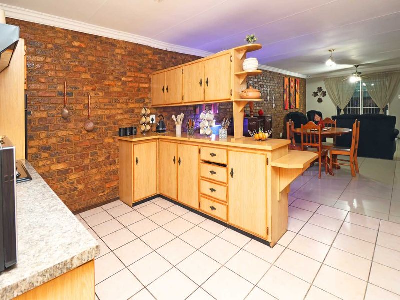Open-plan kitchen and living area featuring exposed brick walls, light wood-tone cabinetry, and neutral ceramic floor tiles throughout the space.