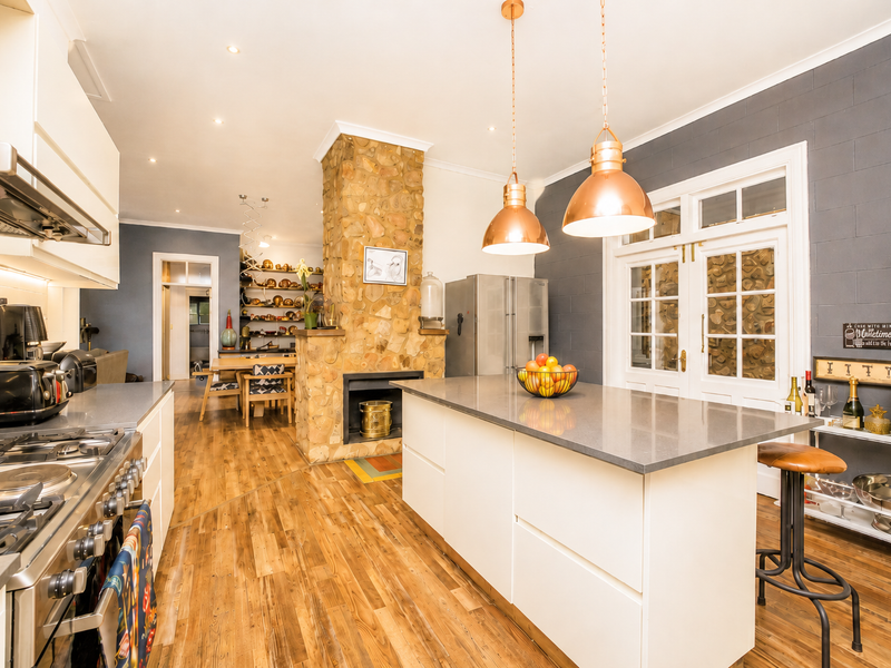 Spacious open-plan kitchen featuring a central island, stone-clad fireplace, modern cabinetry, and high-quality finishes, seamlessly connecting to the dining and living areas.
