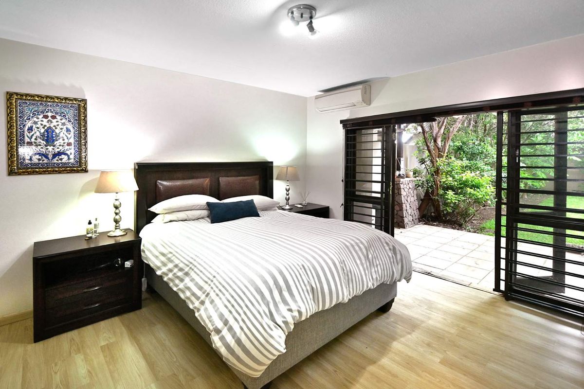 Spacious bedroom featuring light wood-look flooring, a wall-mounted air conditioning unit, and large sliding doors opening onto a private patio and garden area.