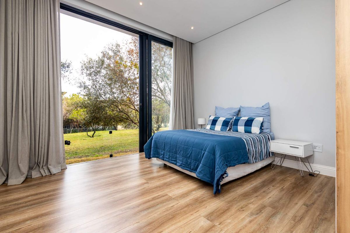 Modern bedroom featuring floor-to-ceiling sliding glass doors that open to a private garden view, complemented by light wood-look flooring and recessed ceiling lighting.