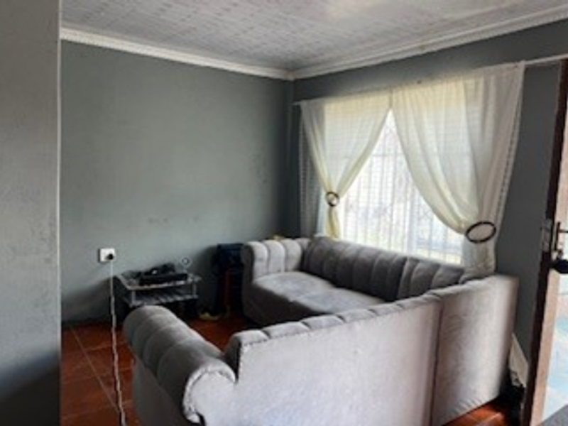 A living room featuring tiled flooring, textured ceiling with cornice, and window security bars, currently finished in a neutral grey tone.