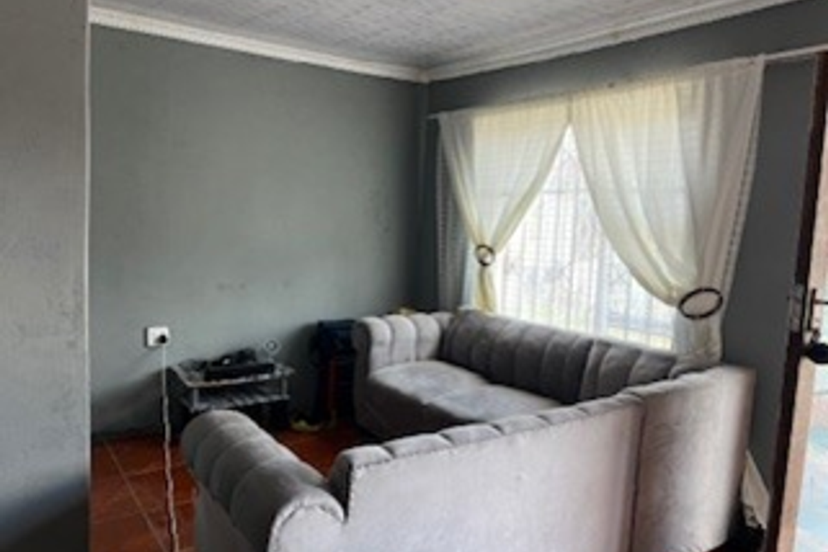 A living room featuring tiled flooring, textured ceiling with cornice, and window security bars, currently finished in a neutral grey tone.