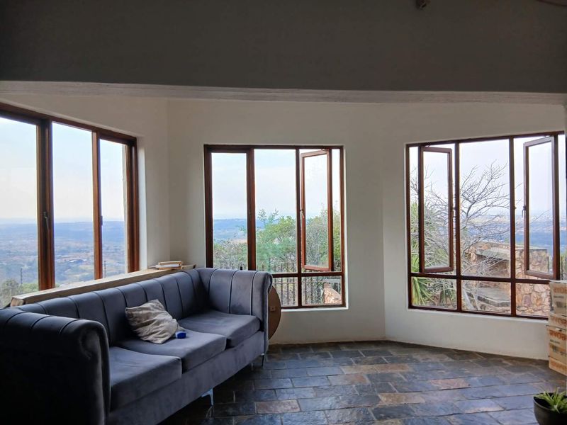 A bright living area featuring slate tile flooring and large timber-framed windows offering expansive views of the surrounding landscape.