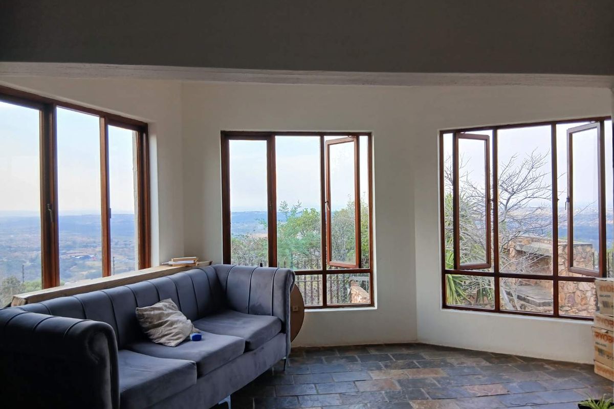 A bright living area featuring slate tile flooring and large timber-framed windows offering expansive views of the surrounding landscape.