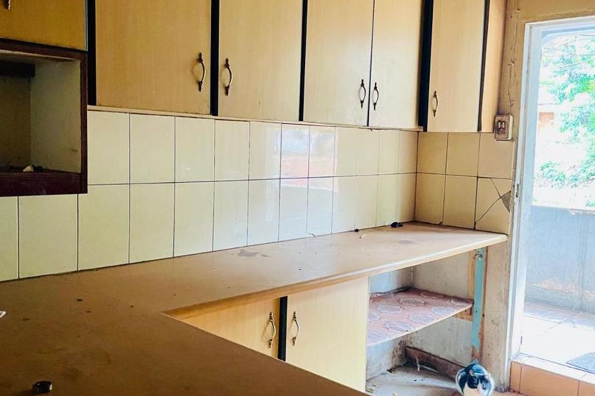A dated kitchen featuring laminate cabinetry, tiled backsplash, and tiled flooring, requiring renovation to modernize the space.
